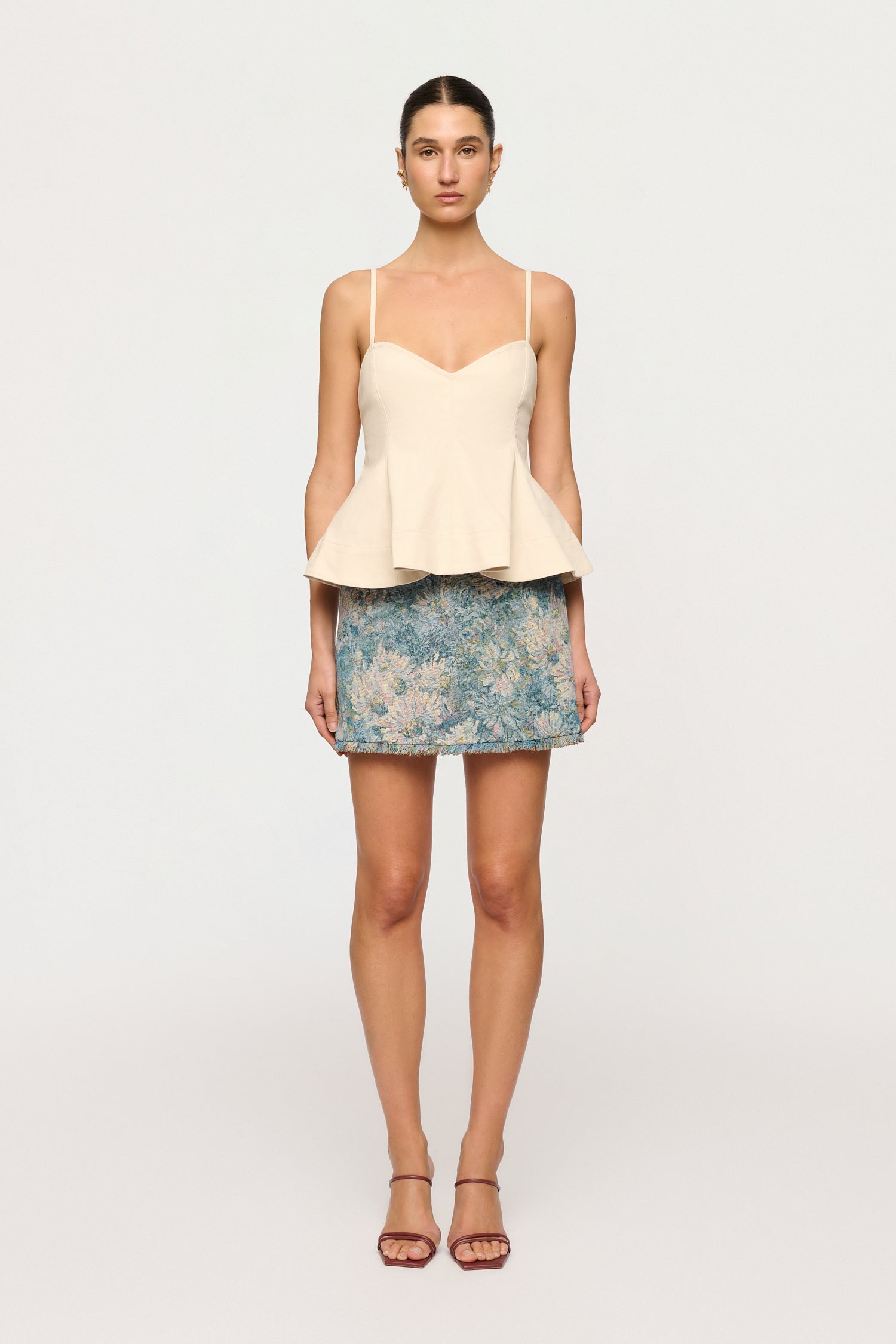 Woman wearing a cream peplum top and floral skirt on a white background