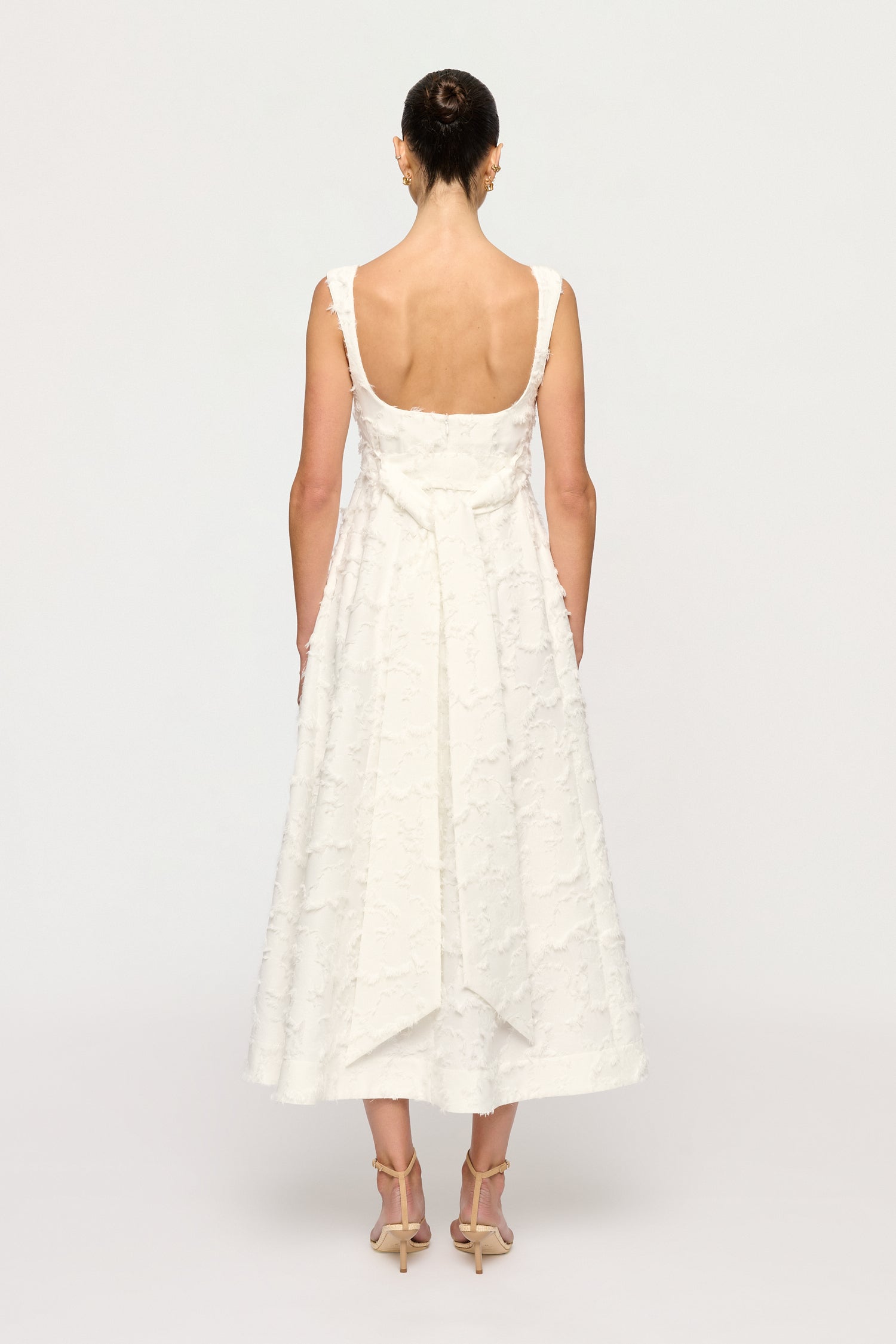 Woman wearing a white Clea dress with floral textured details thin straps on a plain background