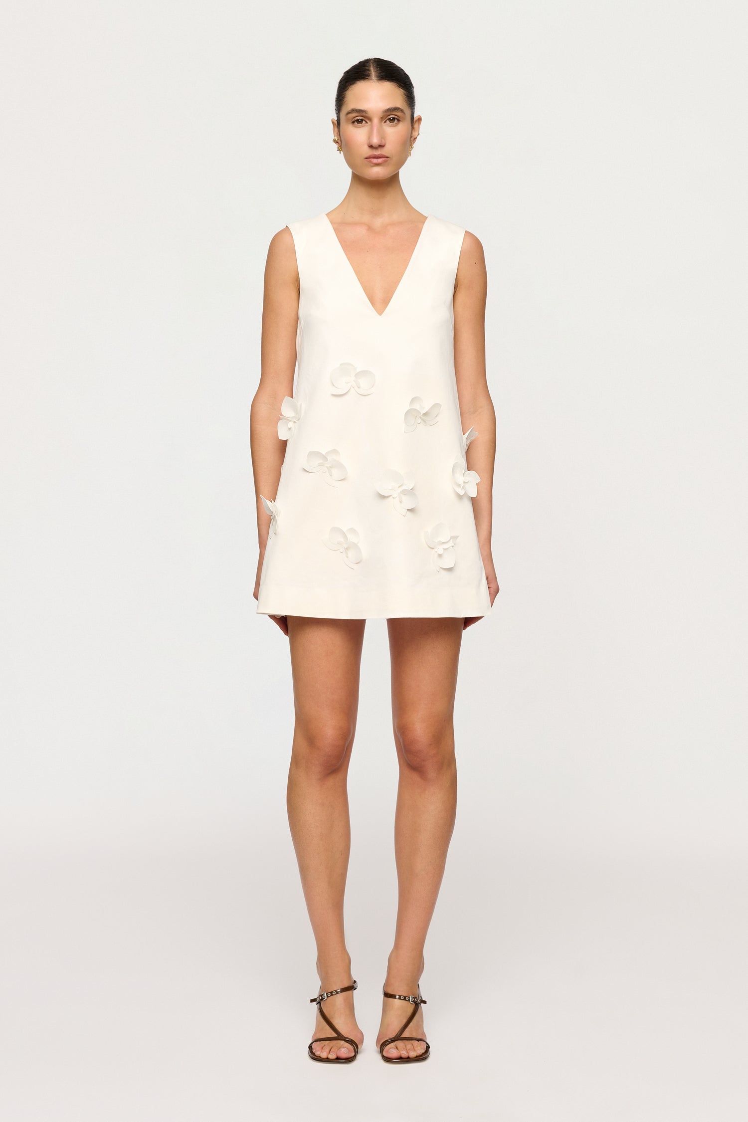 Woman wearing a white dress with floral details on a plain background