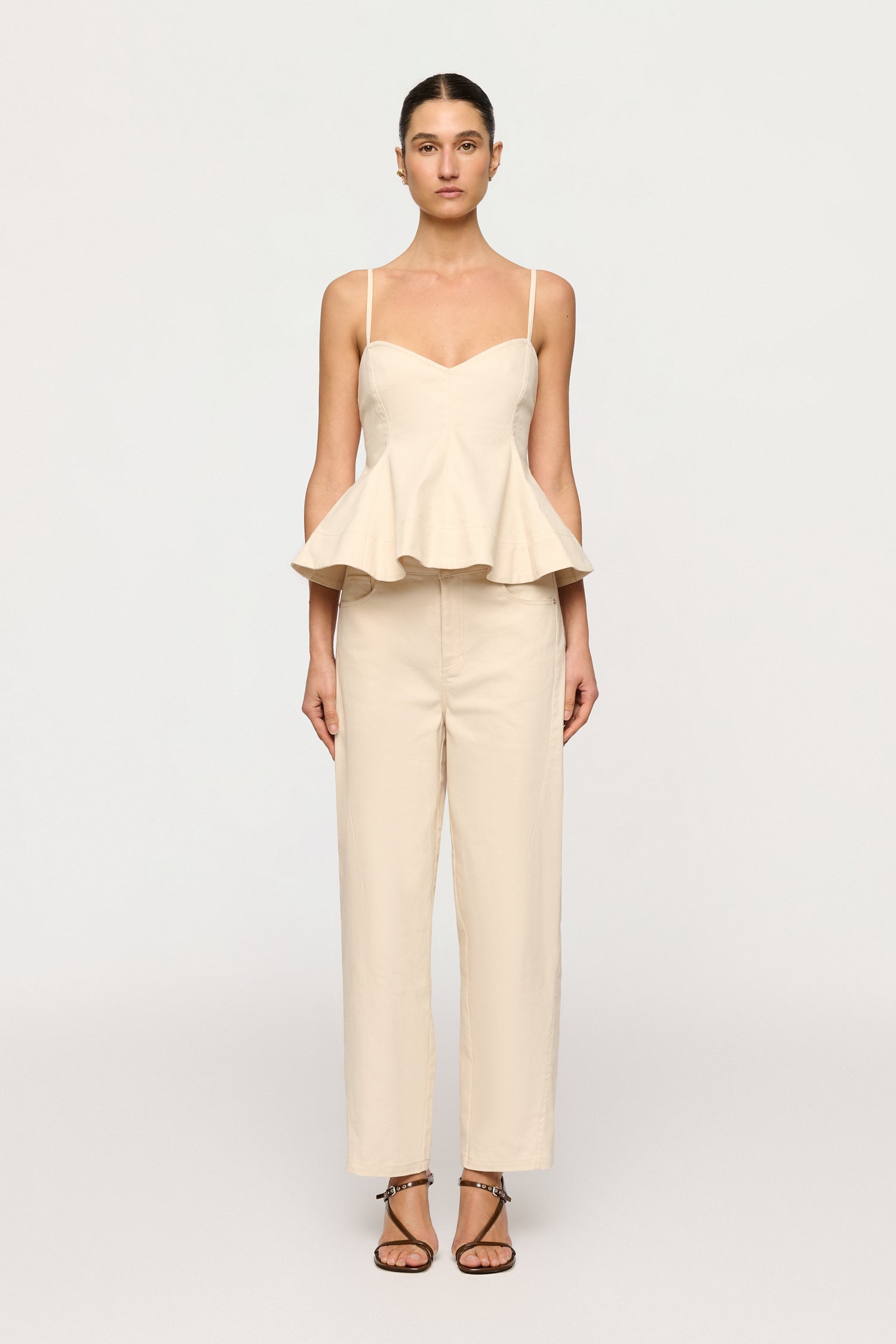 Woman wearing a white peplum top and cream pants on a white background