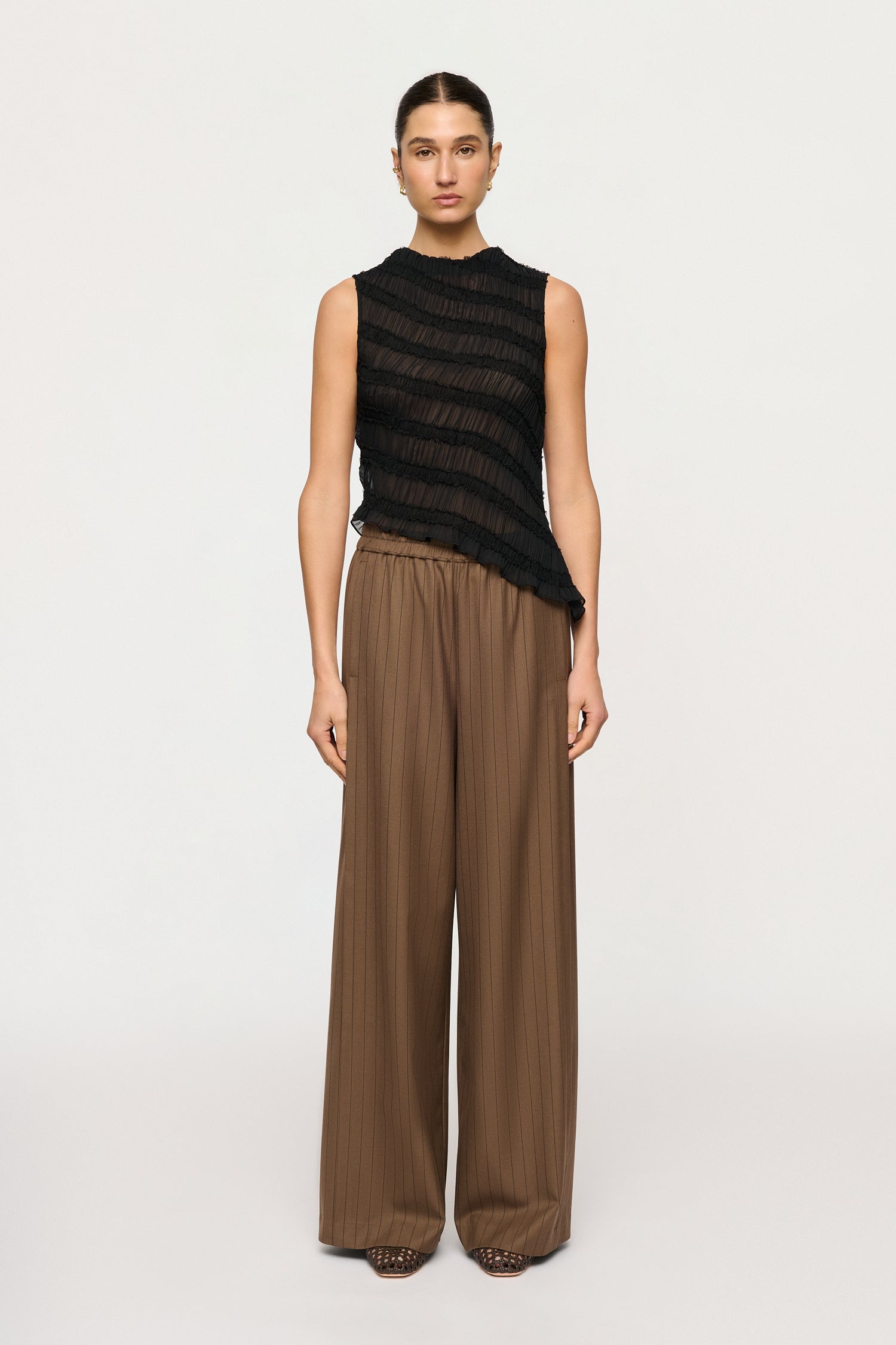 Woman wearing a black sleeveless top and brown wide-leg pants on a white background