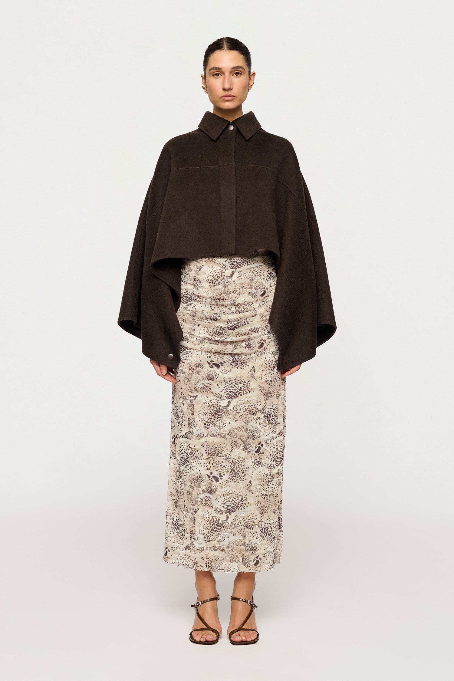 Woman wearing a dark brown cape over a patterned dress on a white background