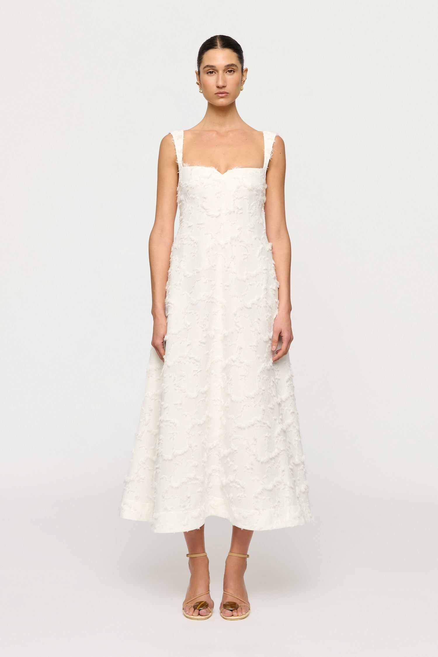 Woman wearing a white Clea dress with floral textured details on a plain background