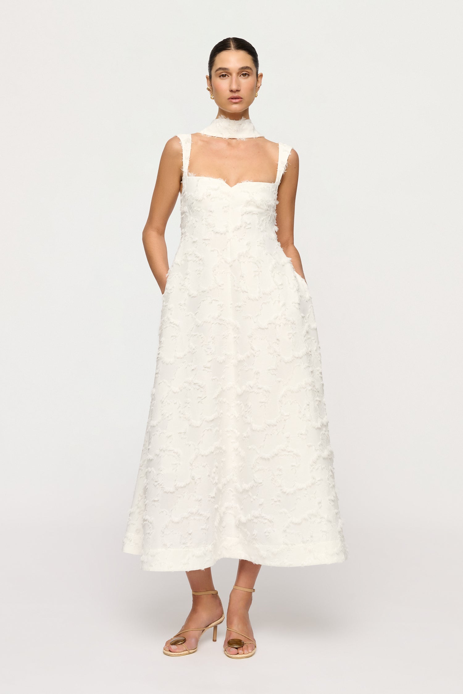 Woman wearing a white Clea dress with floral textured details dress on a plain background