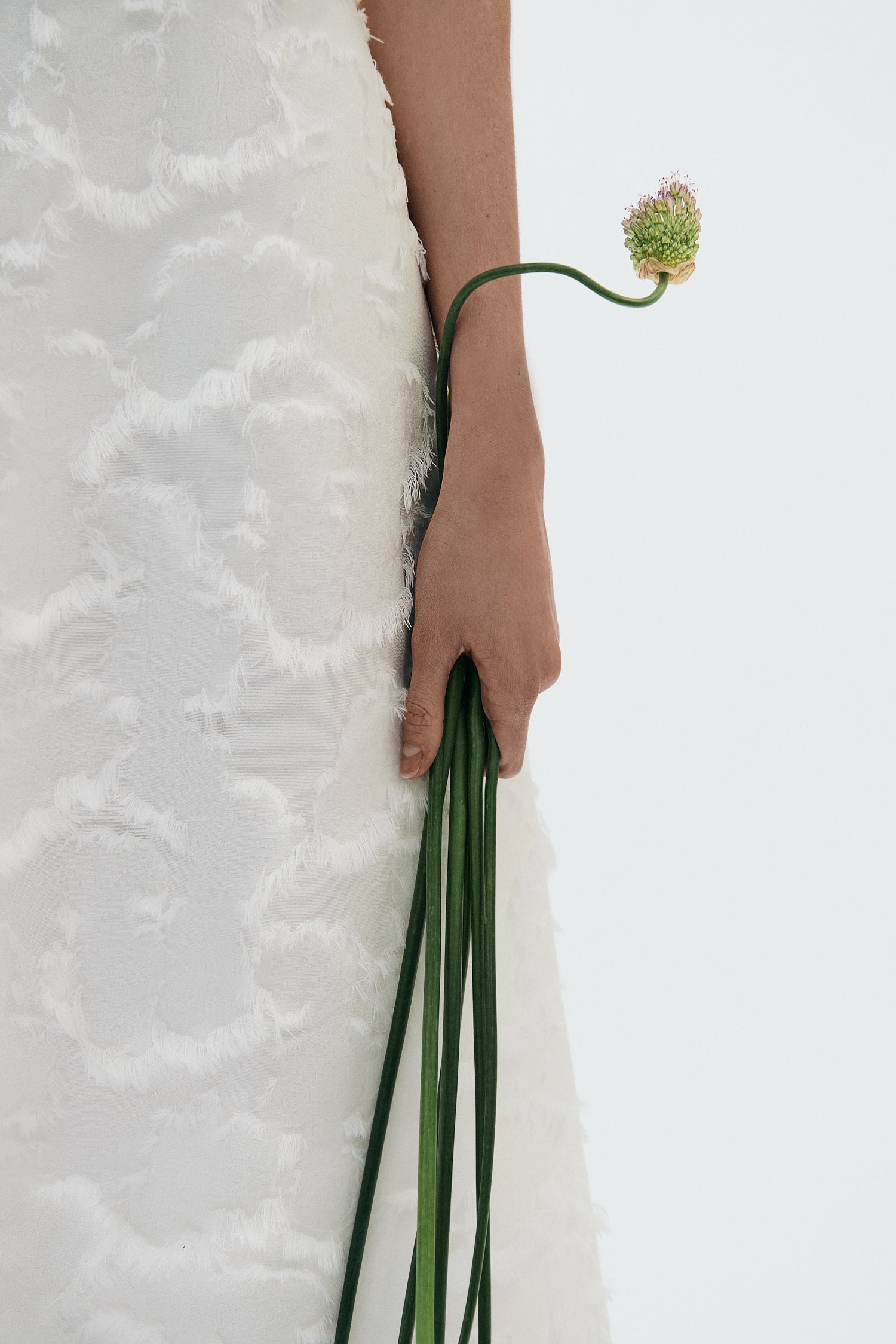 Person holding a bouquet of green flowers against a white background in a white Clea dress with floral textured details