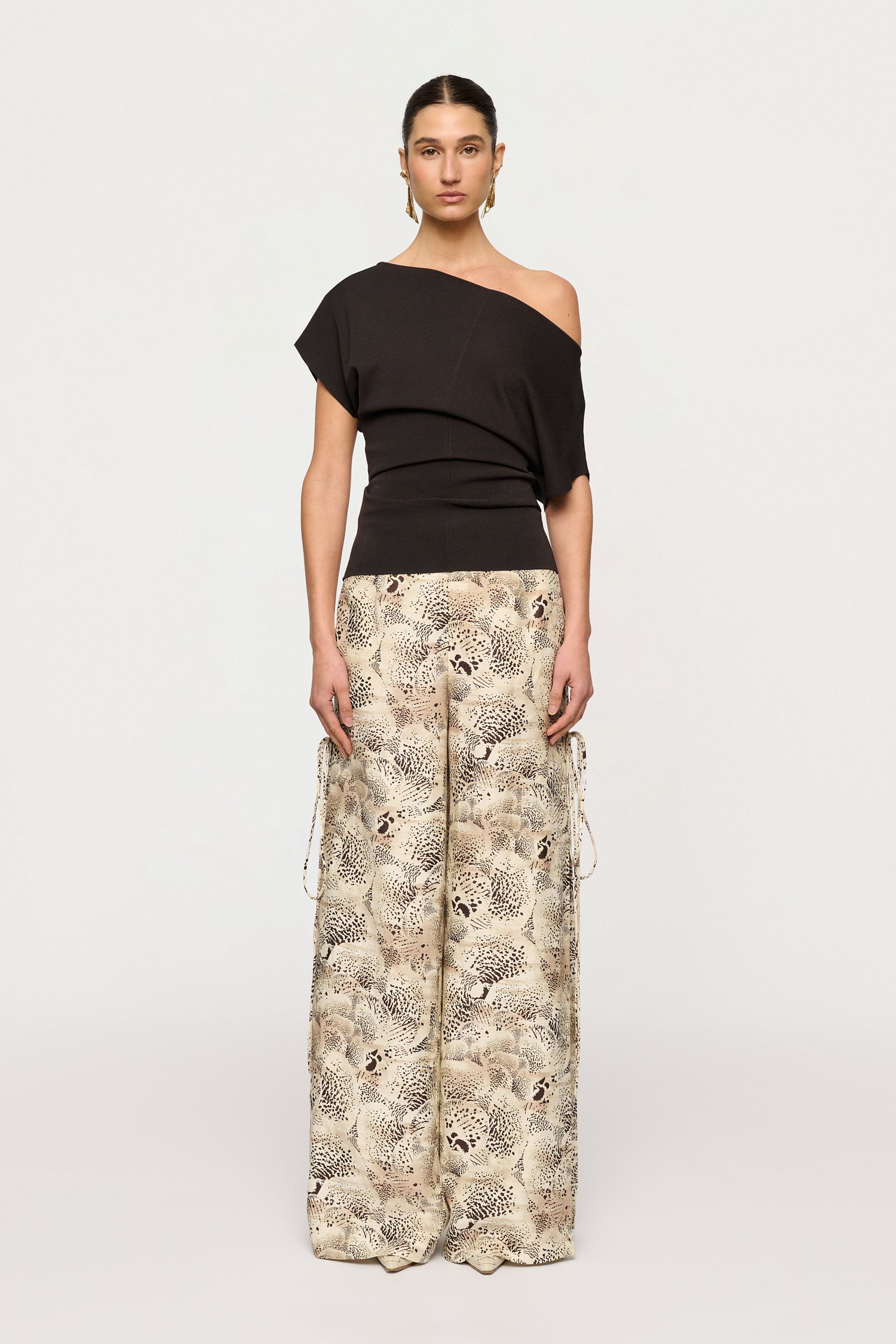 Woman wearing a black off-shoulder top and patterned pants on a white background