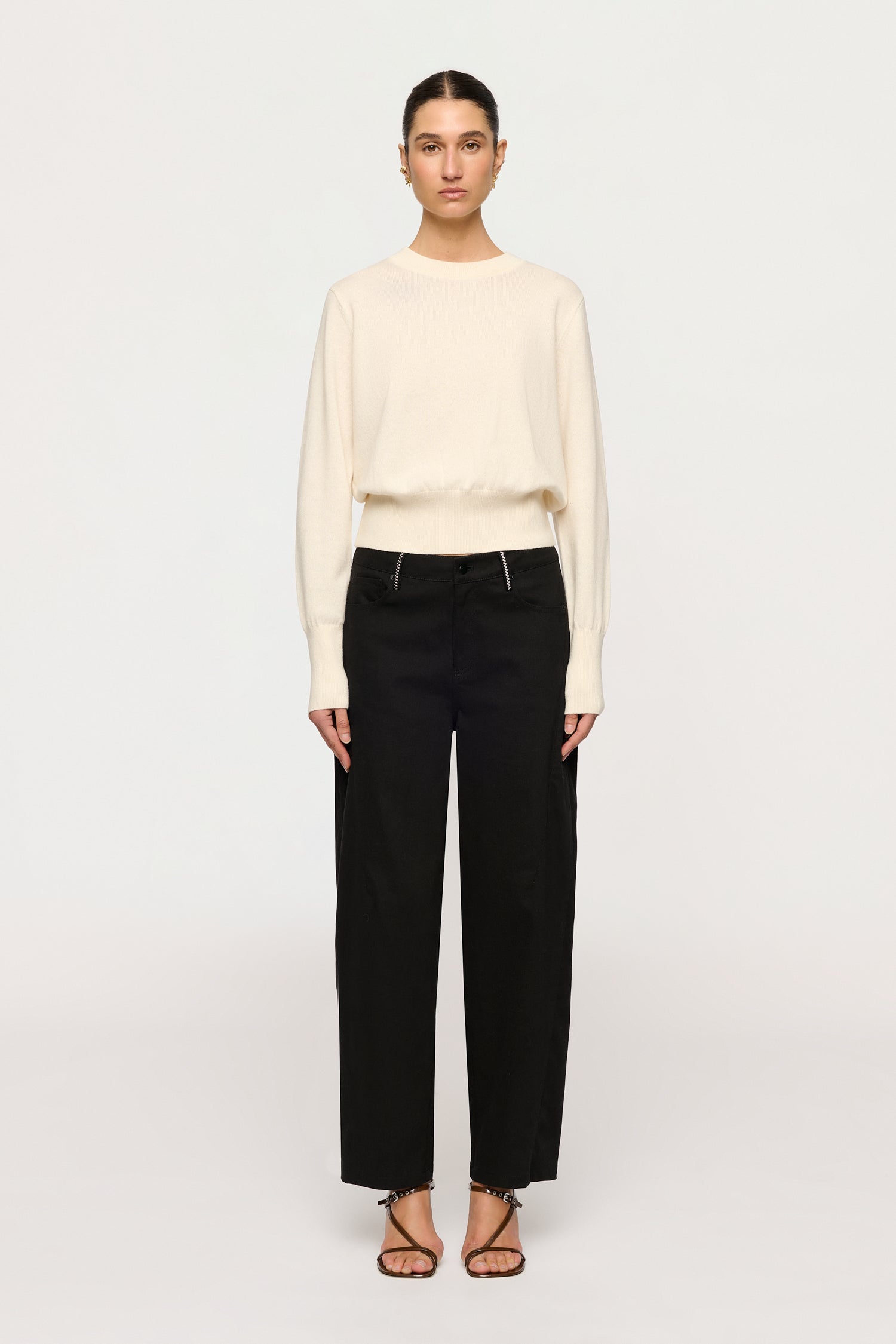 Woman wearing a cream sweater and black pants on a white background